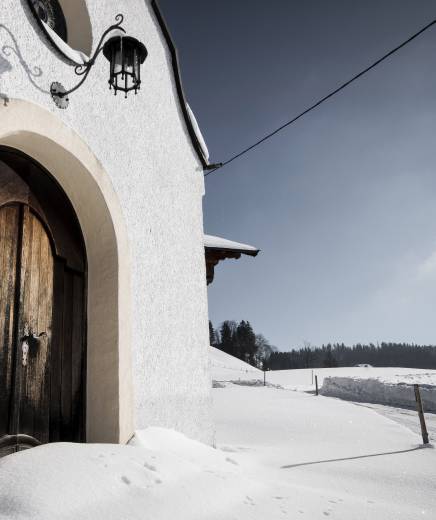 Verschneite Kirche zwischen den Feldern in Erl, Tirol